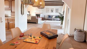 Un comedor con mesa de madera, juegos de mesa y una cocina moderna al fondo.