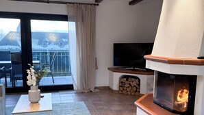Un salón moderno con chimenea, un televisor de pantalla plana y vistas a un paisaje nevado a través de amplios ventanales.