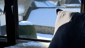 Una ventana con vistas a tejados cubiertos de nieve y el campanario de una iglesia a lo lejos.