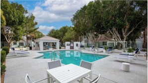 A pool area with lounge chairs, a covered seating area, and a table with chairs.