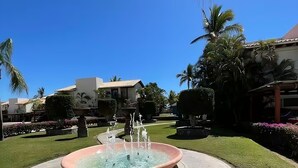 A circular fountain with water jets in the center, surrounded by a paved area with a decorative edge. - Condo. Las Quintas, Terraza, Jardín de Paisaje, Zona de Hoteles, Campo de Golf (San José del Cabo)