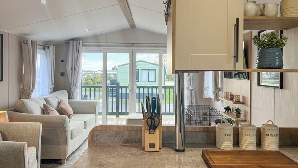 A modern living room with a sofa, a coffee table, and a kitchen area with cabinets and storage containers. - 2 bedroom accommodation in Ashbourne (Ashbourne)