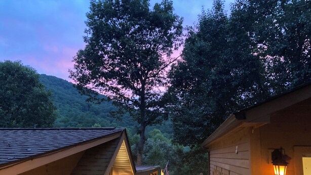 Una cabaña con terraza, paredes de madera y vistas a una ladera boscosa.