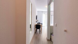Un pasillo estrecho con suelo de madera y paredes blancas que conduce a una habitación con un escritorio y una silla.