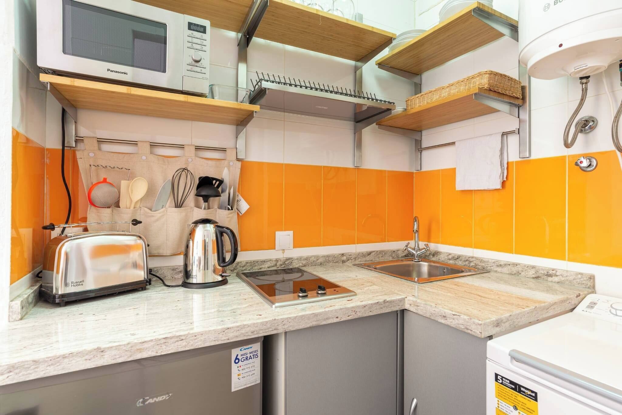 A compact kitchen with a microwave, toaster, kettle, and sink.