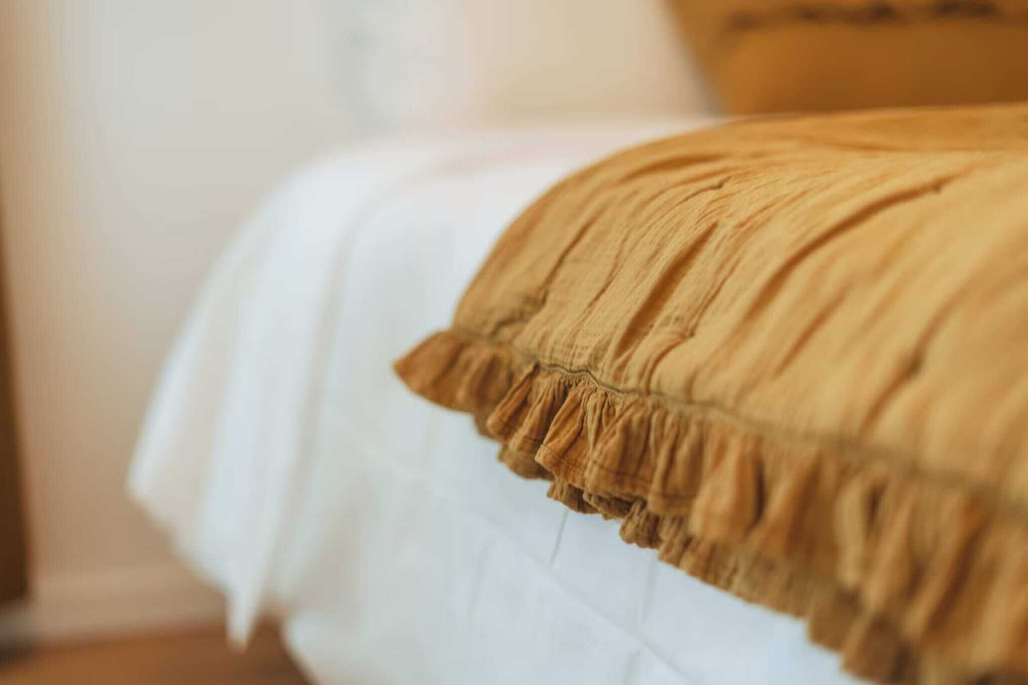 A close-up of a bed with a white sheet and a ruffled, mustard-colored blanket.