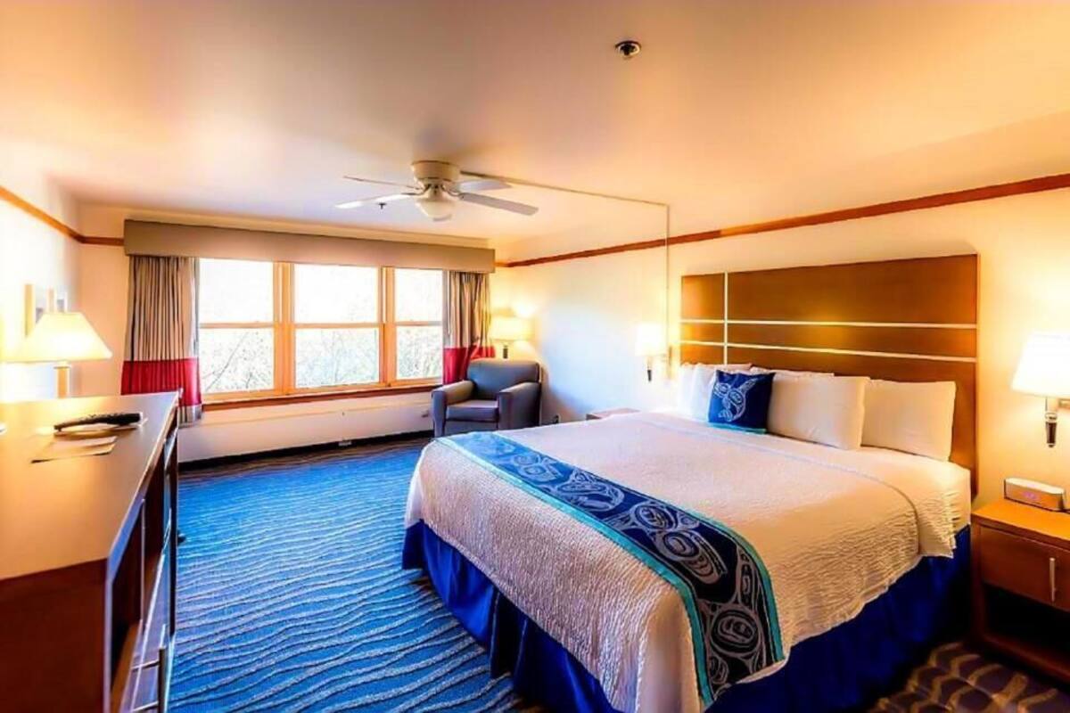 Una habitación de hotel con una cama grande, un escritorio, una silla, un ventilador de techo y una ventana con cortinas.