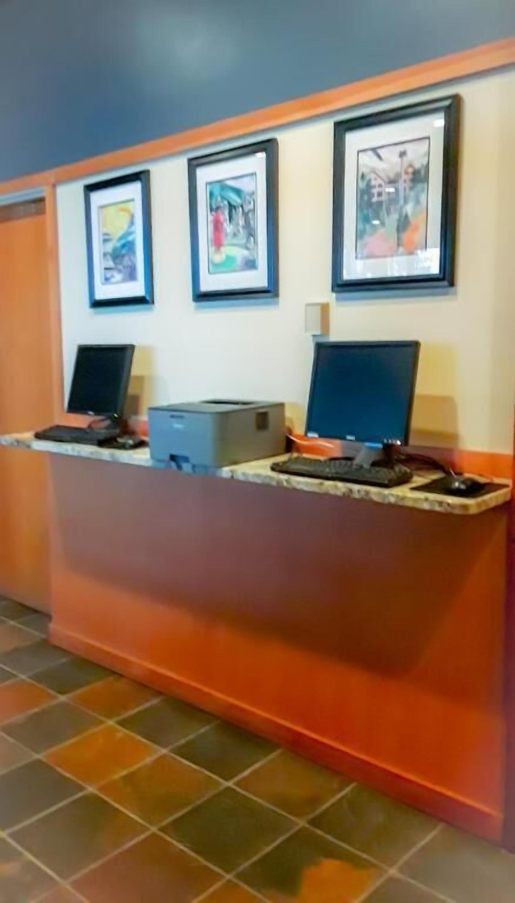 A reception desk with two computers, a printer, and framed artwork on the wall.