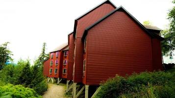 Un edificio rojo de madera con techo inclinado, elevado sobre pilotes, rodeado de vegetación exuberante.