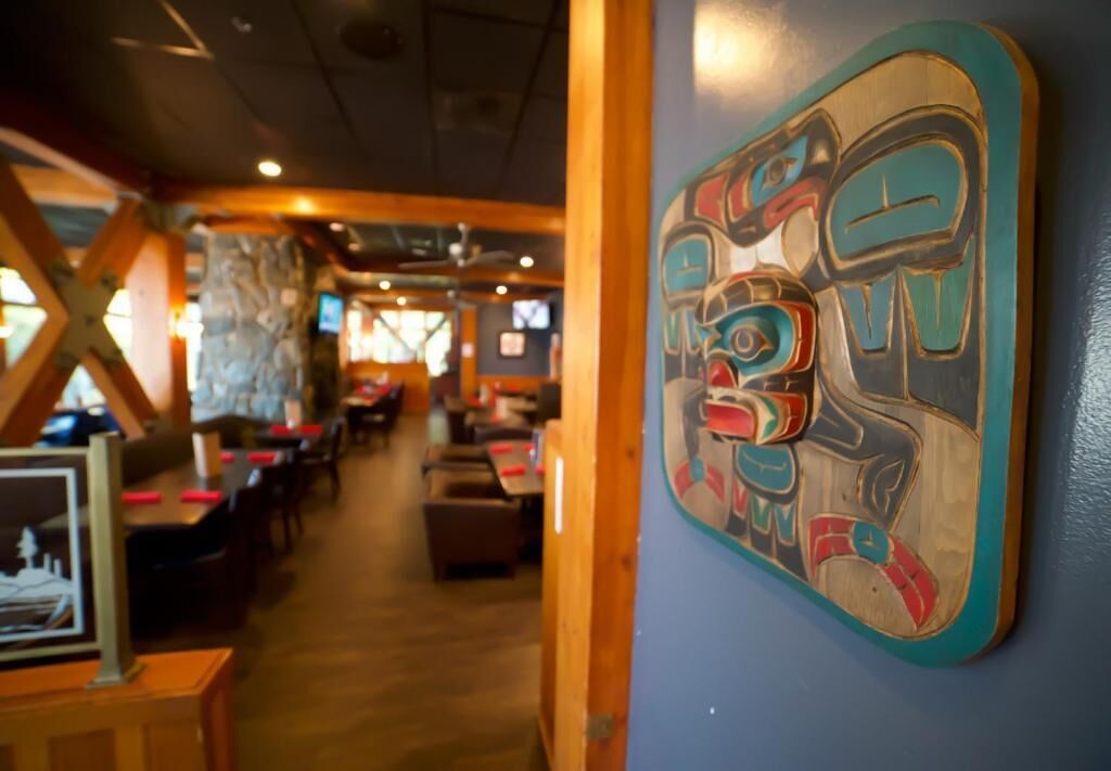 An interior view of a restaurant with wooden tables and chairs, a wall with a colorful artwork, and a stone wall in the background.
