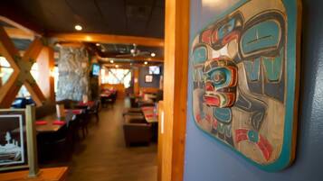 An interior view of a restaurant with wooden tables and chairs, a wall with a colorful artwork, and a stone wall in the background.