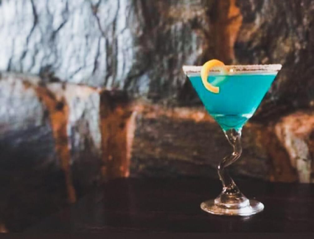 Cocktail-drinkki martini-lasissa, koristeltuna sitruunankuorella, tummalla alustalla.