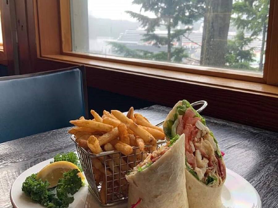 A plate with fries, a sandwich, and a lemon wedge on a table by a window.