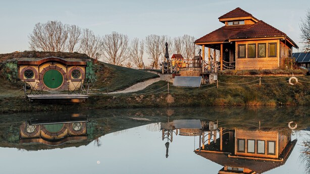 Une maison en bois avec un toit rouge et une porte verte, entourée d’une pelouse et d’arbres.