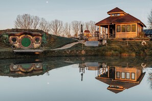 Une maison en bois avec un toit rouge et une porte verte, entourée d’une pelouse et d’arbres.