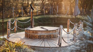 Une terrasse circulaire en bois, délimitée par une barrière en corde, et entourée d’un mur de pierre et d’une clôture.