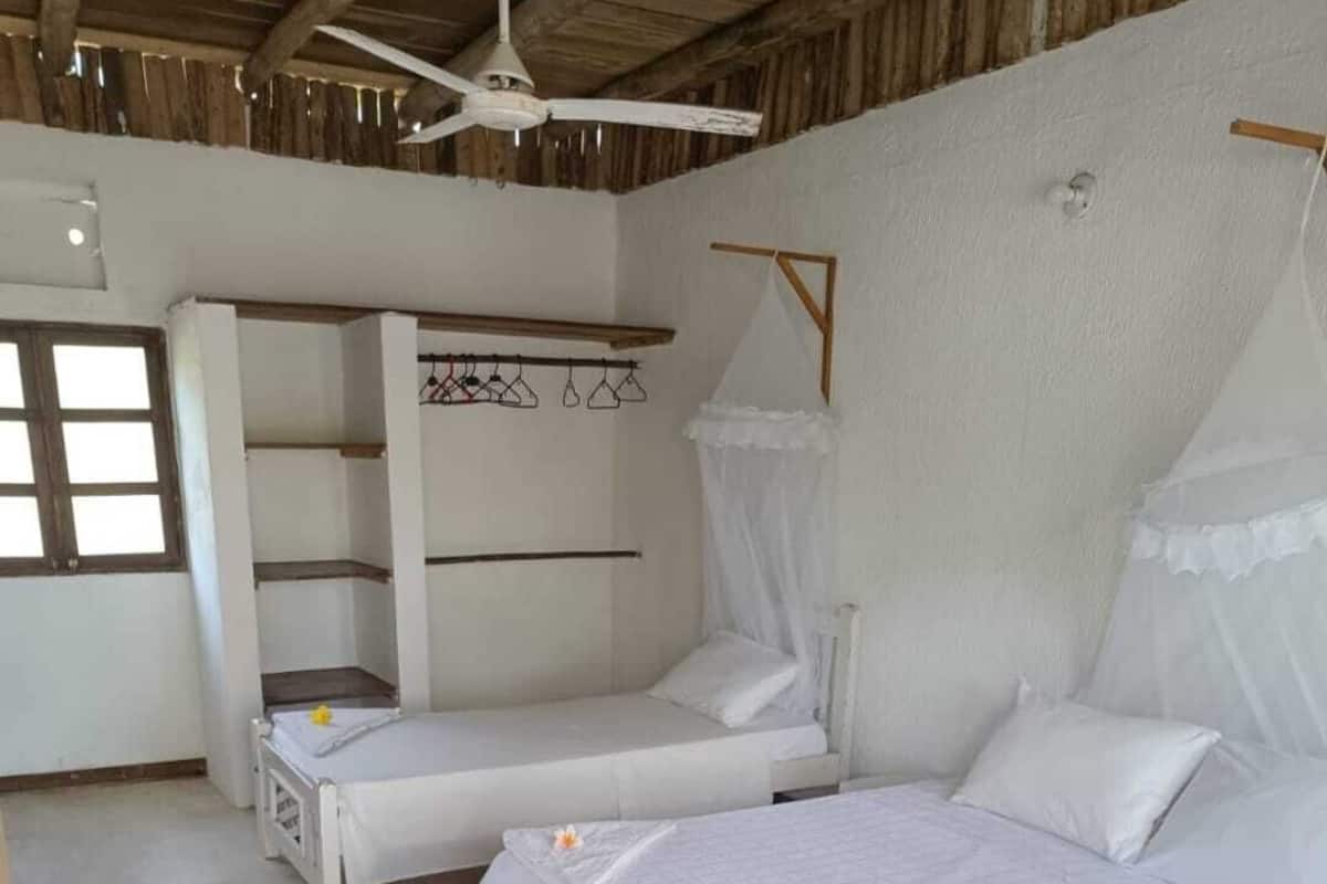 A room with two single beds, a ceiling fan, a wardrobe, and a window.