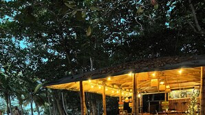 An outdoor dining area with wooden tables and chairs, surrounded by trees. - Santuario Sierra Sagrada (Santa Marta)