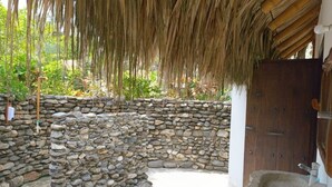 A stone-walled outdoor area with a thatched roof, a wooden door, and a stone sink. - Santuario Sierra Sagrada (Santa Marta)
