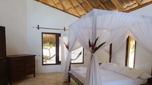 A bedroom with a bed under a canopy, a wooden dresser, a red rug, and a window with a view of a tree and hammock. - Santuario Sierra Sagrada (Santa Marta)