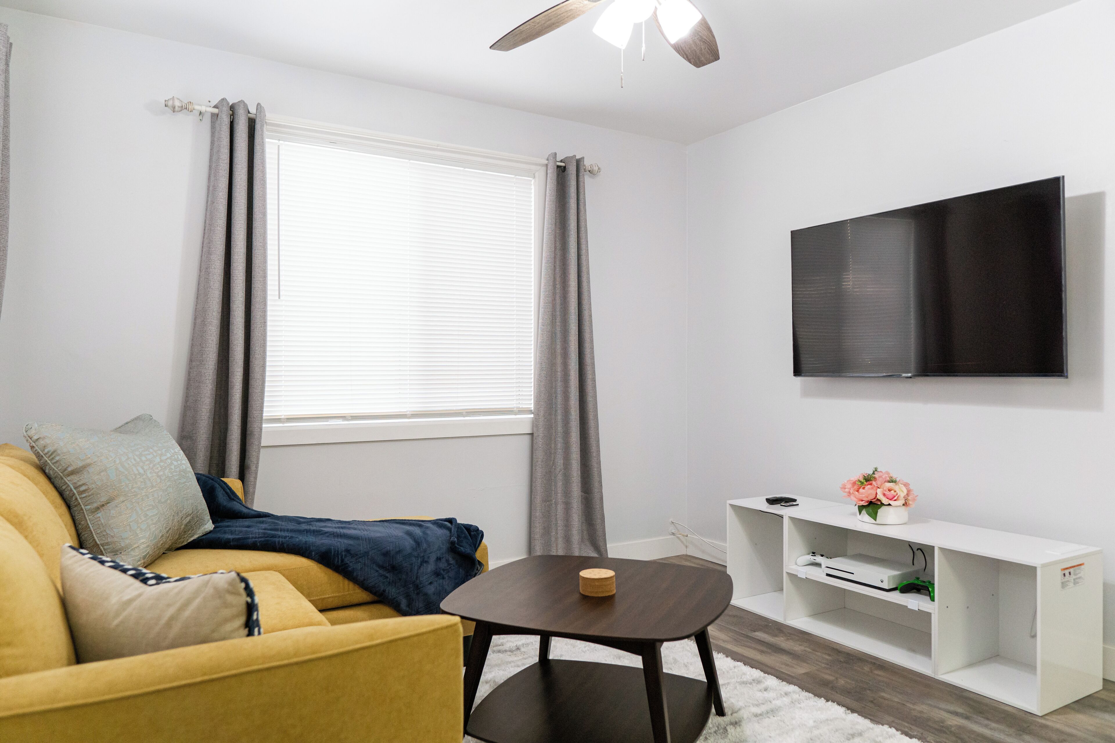 Una sala de estar moderna con un sofá, una mesita, un televisor y un mueble bajo con un jarrón de flores.