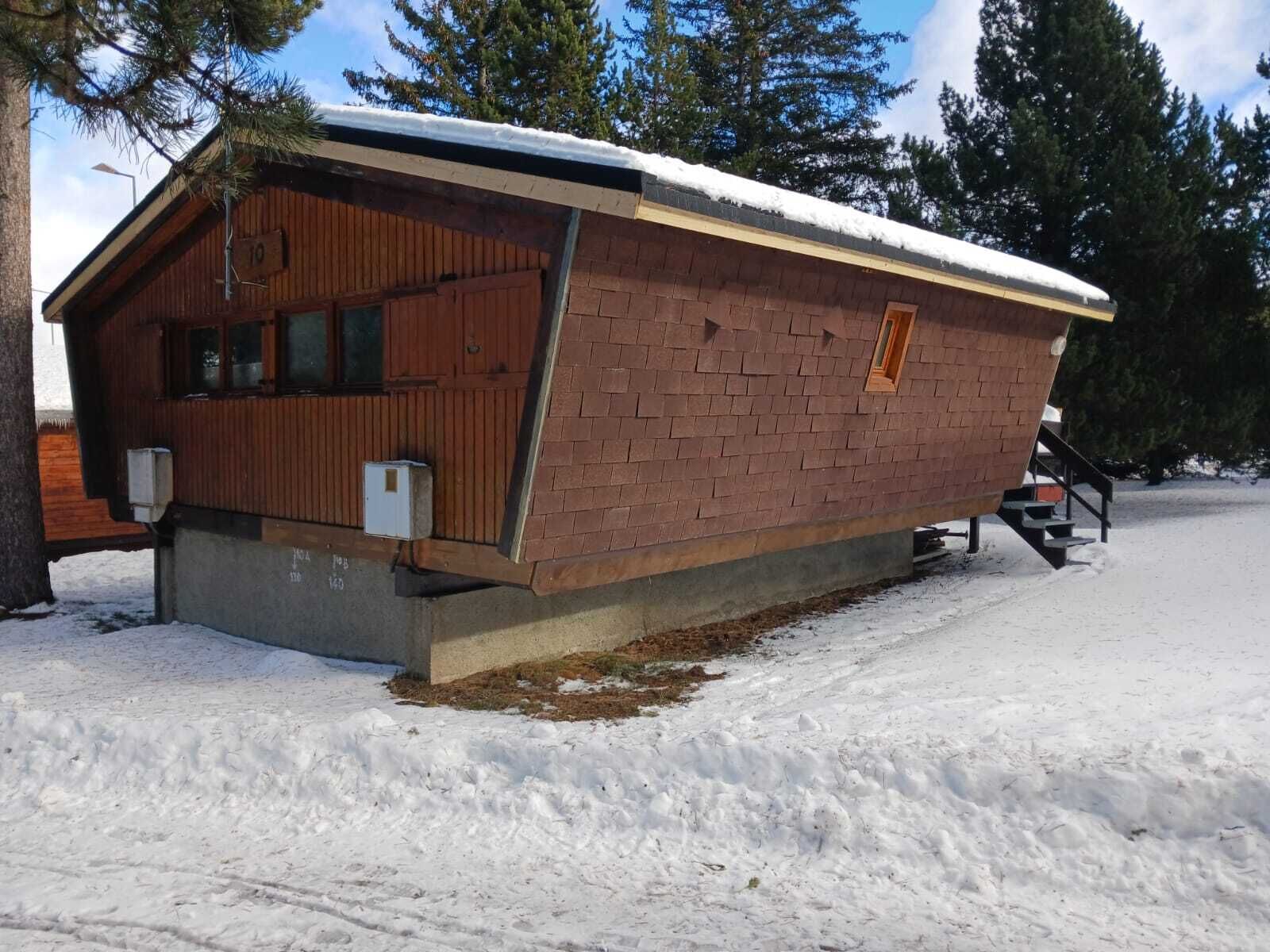 A wooden cabin with a brick extension, a covered porch, and a snow-covered roof.