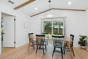 Un coin repas avec une table et des chaises en bois, un luminaire suspendu et une vue sur l’extérieur grâce à une porte vitrée.