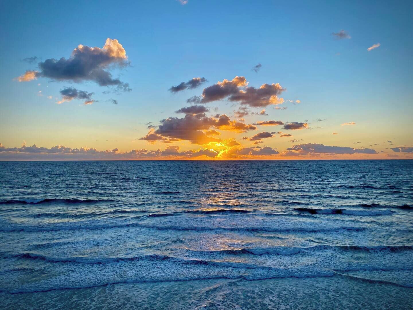 A sunset over the ocean with waves and clouds.