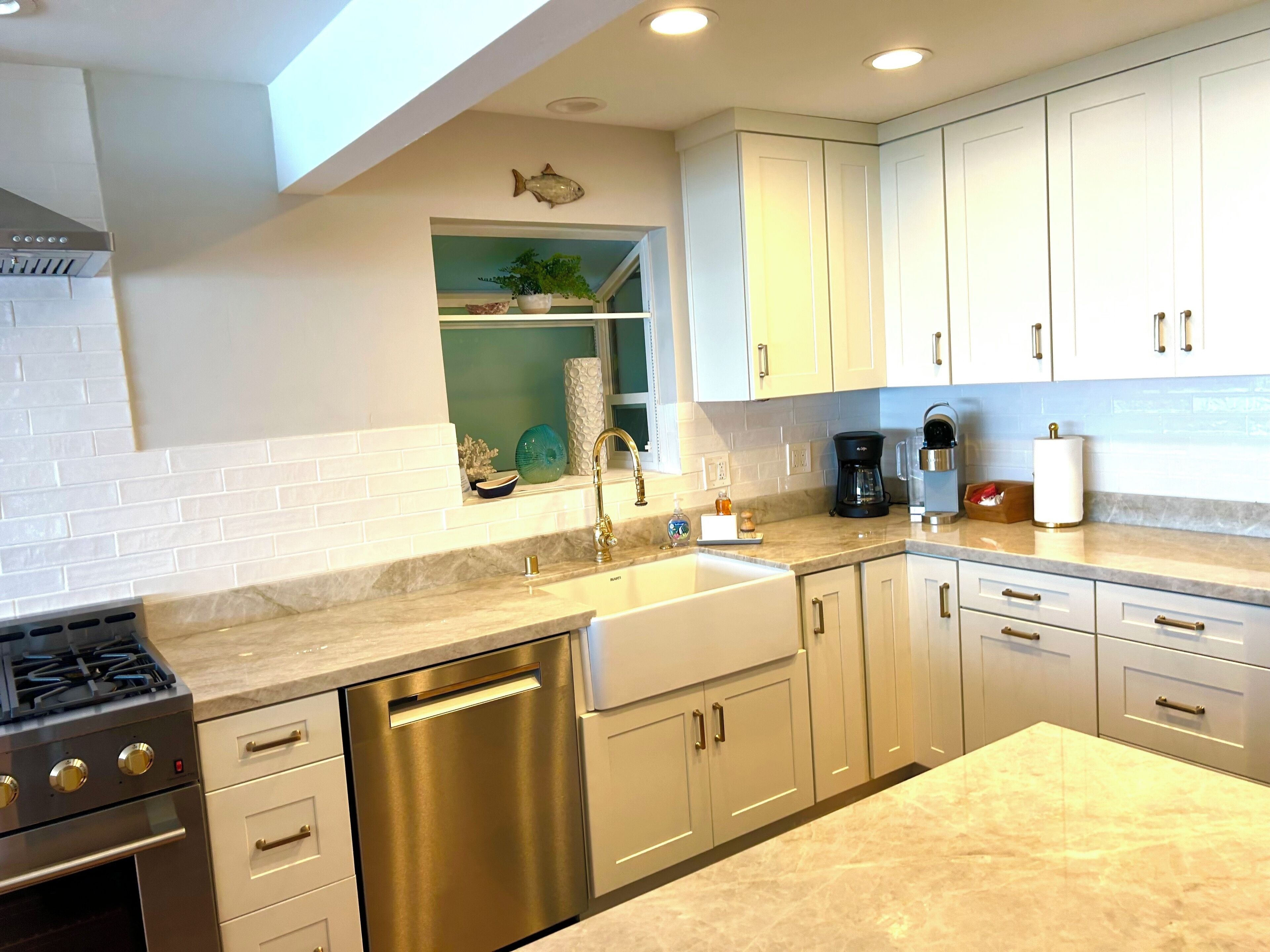 A modern kitchen with white cabinets, a stainless steel dishwasher, a gas stove, and a coffee maker.