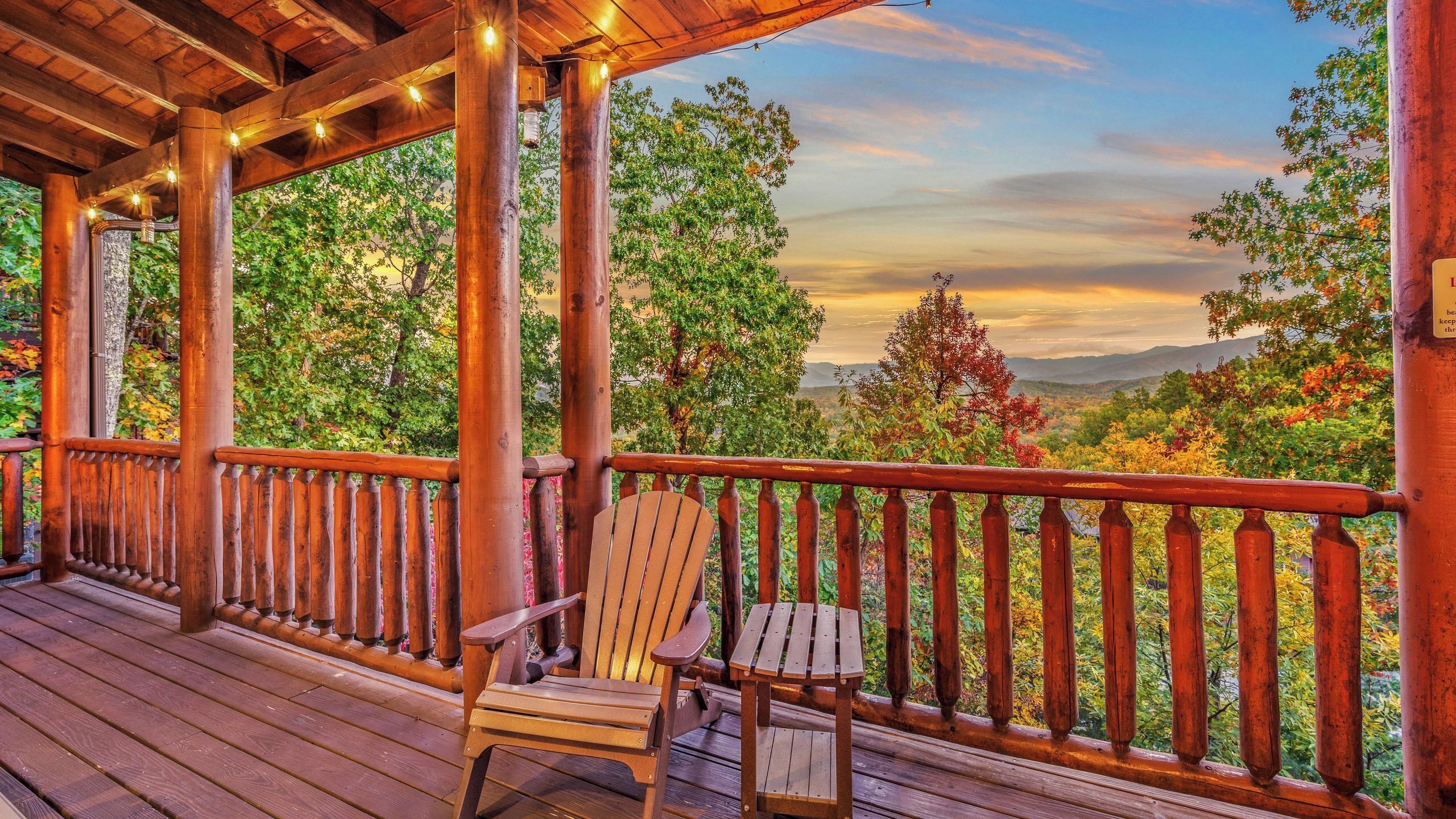 A wooden deck with a wooden chair and a railing, overlooking a scenic landscape with trees and mountains.