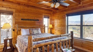 A wooden cabin bedroom with a bed, a ceiling fan, and a window with a mountain view. - A View for All Seasons by Avantstay 12bdr w/ Game Room, Hot Tub, Movie Theater, Deck Views (Sevierville)