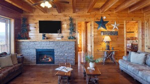 A cozy log cabin interior with a stone fireplace, wooden furniture, and a television mounted on the wall. - A View for All Seasons by Avantstay 12bdr w/ Game Room, Hot Tub, Movie Theater, Deck Views (Sevierville)