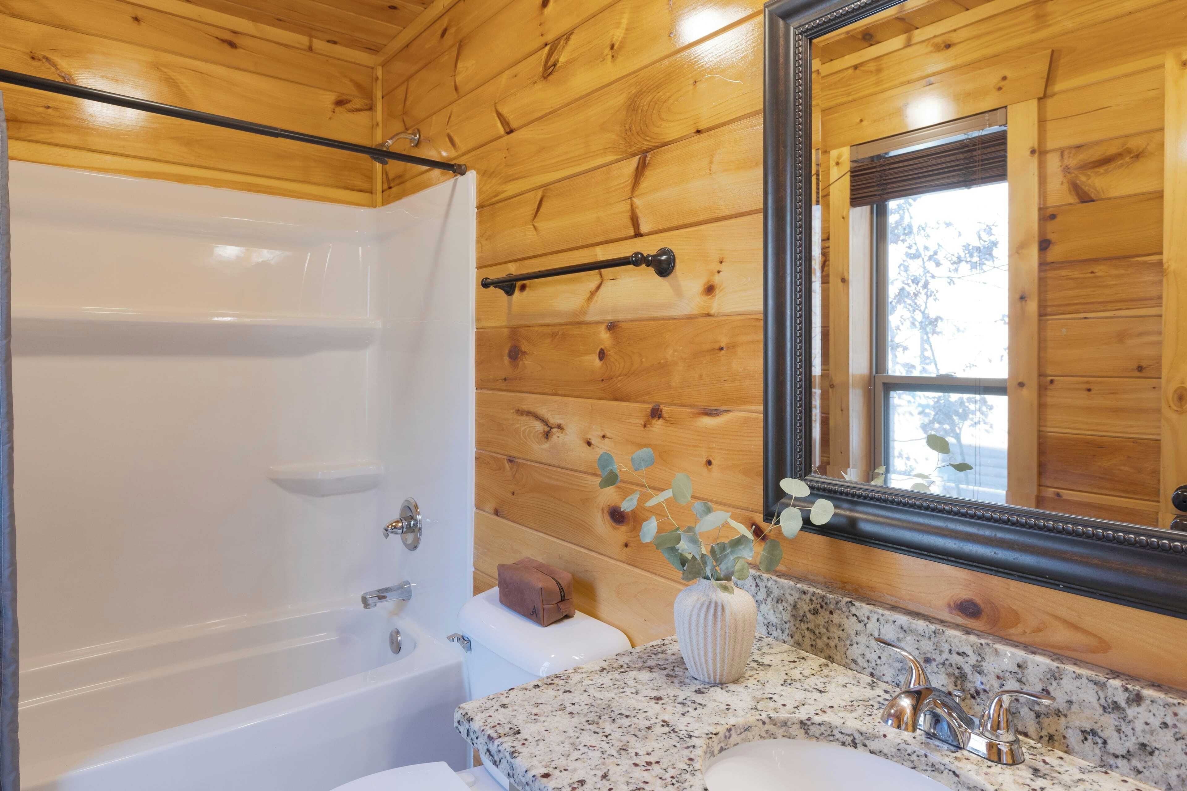 Une salle de bain avec des murs en bois, une baignoire blanche, un lavabo doté d’un plan de travail en marbre et un miroir avec un cadre en bois.