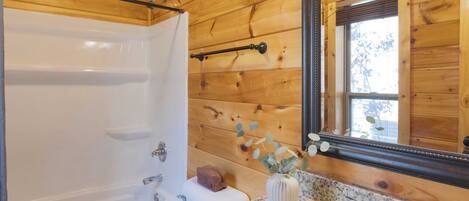 Une salle de bain avec des murs en bois, une baignoire blanche, un lavabo doté d’un plan de travail en marbre et un miroir avec un cadre en bois.
