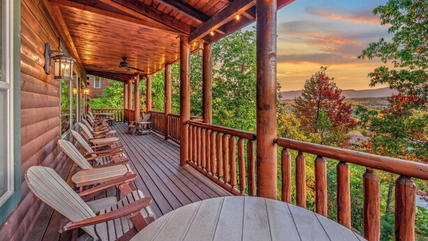 A wooden deck with chairs and a table, overlooking a scenic landscape with trees and mountains. - A View for All Seasons by Avantstay 12bdr w/ Game Room, Hot Tub, Movie Theater, Deck Views (Sevierville)