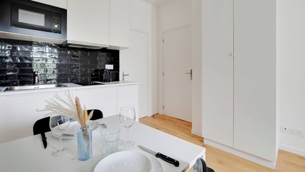 A modern kitchen with white cabinetry, a black microwave, and a black backsplash. - Studio Moderne - 2P- Nanterre (Nanterre)