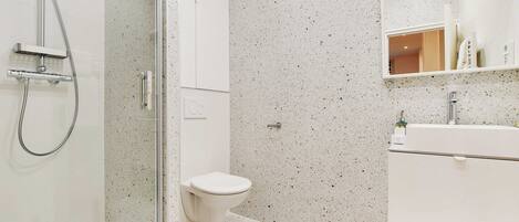 Une salle de bain moderne avec une douche à parois de verre, des toilettes blanches et un lavabo blanc avec un miroir au-dessus.