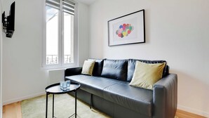 A modern living room with a black leather sofa, a small round table, and a framed abstract art piece on the wall. - Studio Moderne - 2P- Nanterre (Nanterre)