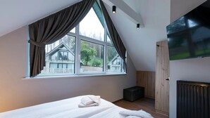 A bedroom with two beds, a large window with curtains, a TV, and a radiator. - Premium Chalet in Buntenbock (Clausthal-Zellerfeld)