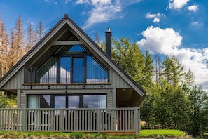 Une cabane moderne à deux étages, dotée d’un balcon, de grandes fenêtres et d’une cheminée.