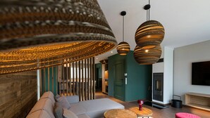 A modern living room with a large sofa, two wooden side tables, a red ottoman, and a large woven light fixture. - Premium Chalet in Buntenbock (Clausthal-Zellerfeld)