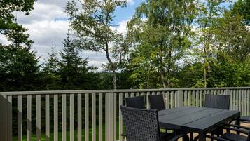 A deck with a table and chairs, surrounded by a wooden railing and trees.