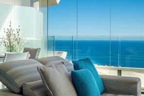 Un balcon avec vue sur l’océan, un canapé agrémenté de coussins à motifs et une plante en pot.