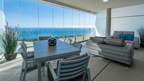 A modern living room with a large glass wall, a dining area, and a sofa with cushions. - Apartment 'Stupa Hills - Spectacular Sea Views' with Sea View, Wi-Fi and Air Conditioning (Benalmadena)