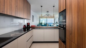 A modern kitchen with wooden cabinets, a black countertop, and a view of the living area. - Apartment 'Stupa Hills - Spectacular Sea Views' with Sea View, Wi-Fi and Air Conditioning (Benalmadena)