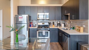 Una cocina moderna con armarios oscuros, electrodomésticos de acero inoxidable y una mesa de comedor de vidrio.