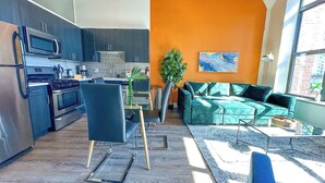 Una cocina moderna con electrodomésticos de acero inoxidable, un comedor con una silla azul y una sala de estar con un sofá verde y paredes anaranjadas.