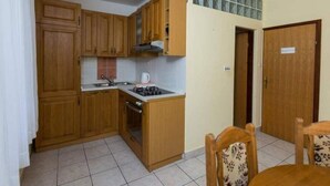 Cocina compacta con armarios de madera, estufa a gas y pileta. Zona de comedor con mesa y sillas.