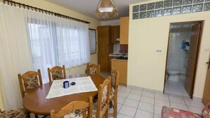 Un comedor con una mesa y sillas de madera, una cocina al fondo y la puerta de un baño.