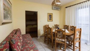 Un comedor con una mesa y sillas, un sofá, un ventilador de techo y una ventana con cortinas.